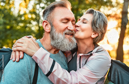 Elderly beautiful couple with gray hair enjoying quality and active time together after retirement. Portrait of two older people, a woman kisses and hugs a man with his eyes closed. Romantic senior. © HBS