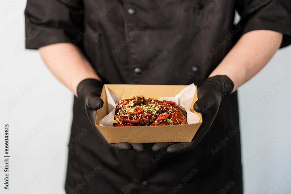 The cook holds in his hands a box with grilled spicy chicken