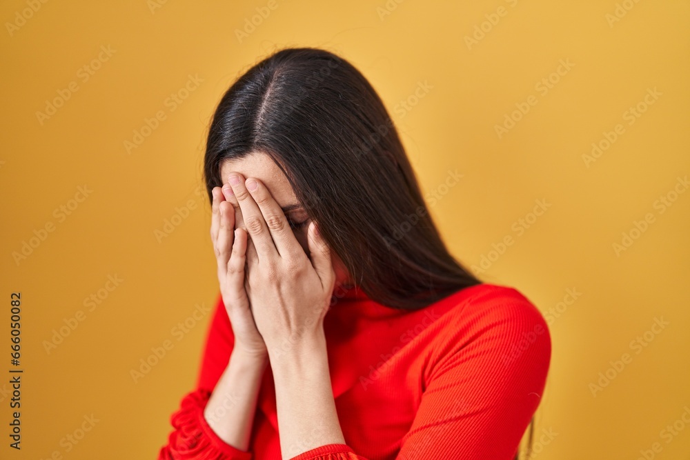 Young hispanic woman standing over yellow background with sad expression covering face with hands while crying. depression concept. Young hispanic woman standing over yellow background with sad expression covering face with hands while crying. depression concept.