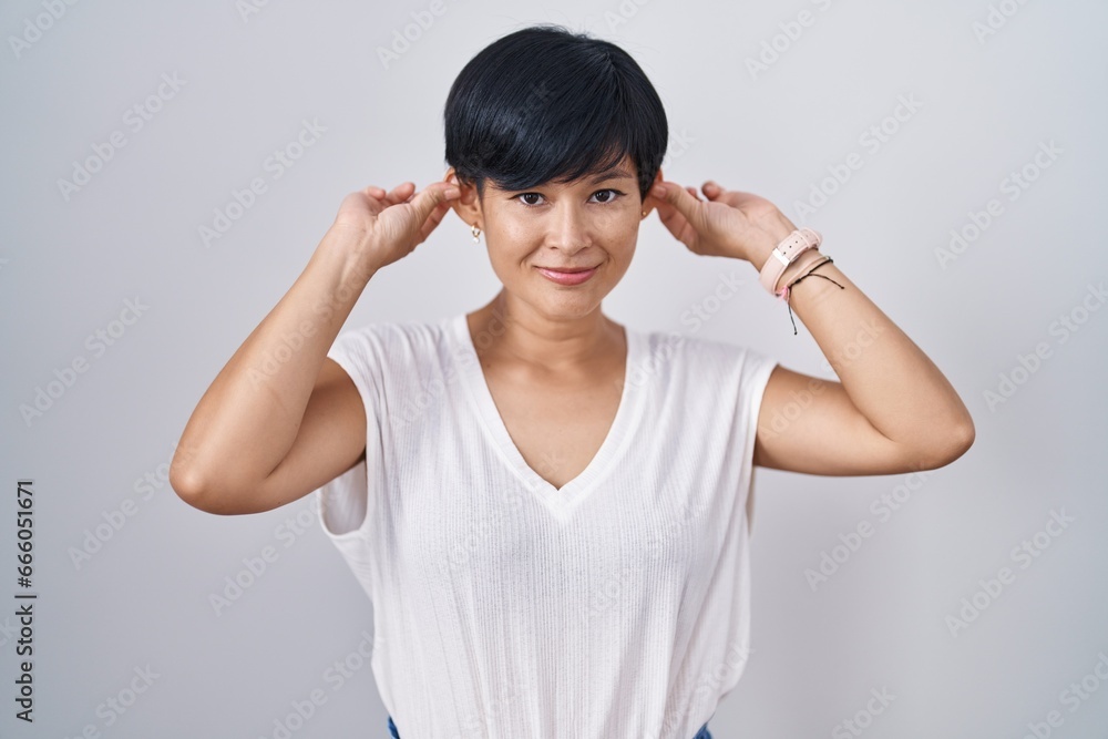 Young asian woman with short hair standing over isolated background smiling pulling ears with fingers, funny gesture. audition problem Young asian woman with short hair standing over isolated background smiling pulling ears with fingers, funny gesture. audition problem