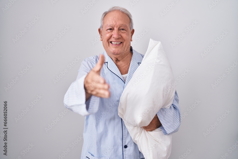 Senior man with grey hair wearing pijama hugging pillow smiling friendly offering handshake as greeting and welcoming. successful business. Senior man with grey hair wearing pijama hugging pillow smiling friendly offering handshake as greeting and welcoming. successful business.
