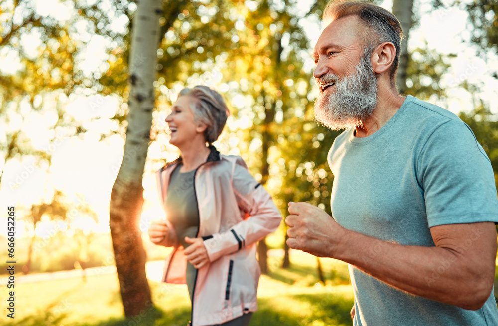 Fototapeta premium Healthy routine. Spirited pensioners leading active lifestyle and running every morning on fresh air. Determined smiling spouses dressed in sport outfits doing cardio for improving heart rate.