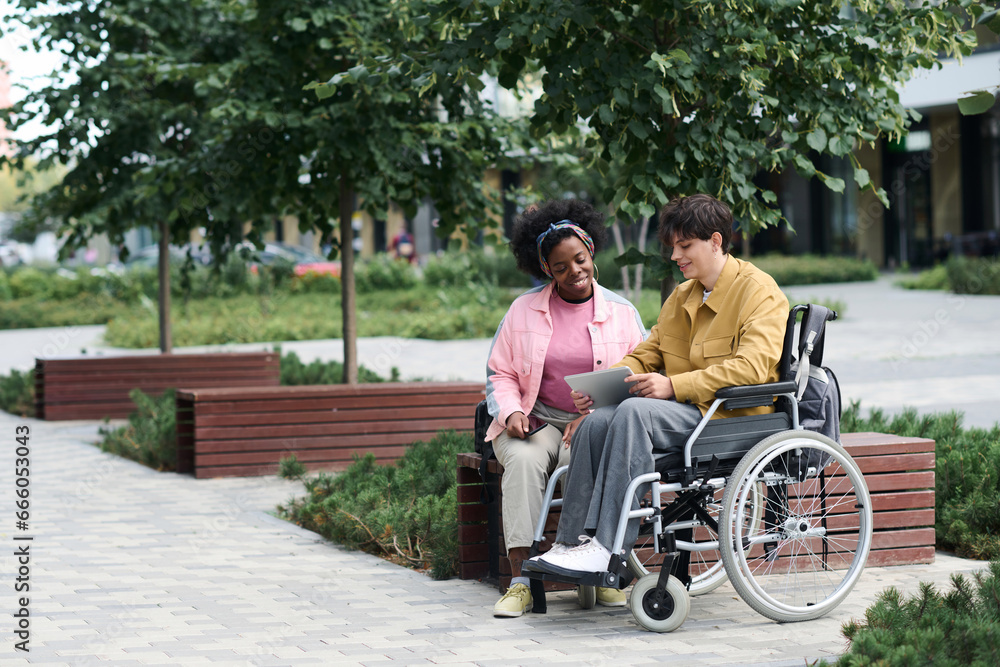 Man with disability spending time outdoors with friend, they using digital tablet and watching funny video Man with disability spending time outdoors with friend, they using digital tablet and watching funny video