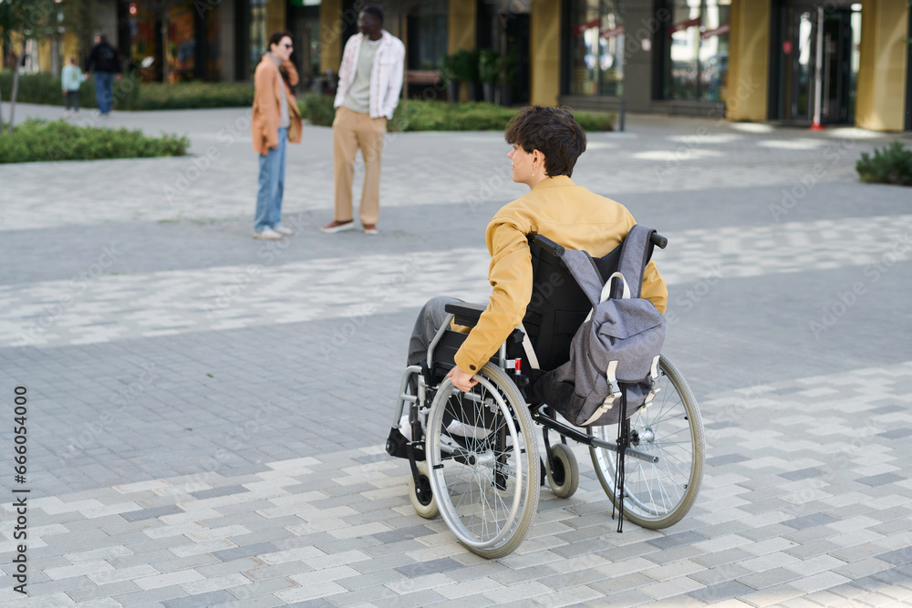 Rear view of young man with disability moving in wheelchair in the city