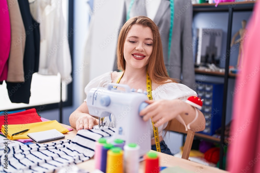 Young redhead woman tailor smiling confident using sewing machine at clothing factory Young redhead woman tailor smiling confident using sewing machine at clothing factory