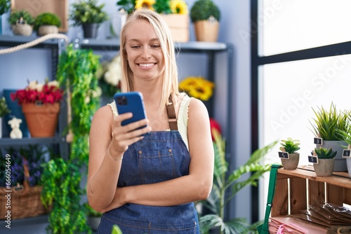 Young blonde woman florist smiling confident using smartphone at florist store
