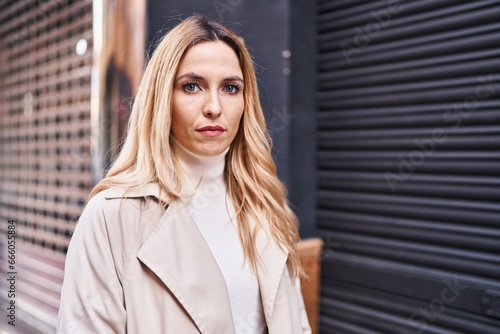 Young blonde woman standing with serious expression at street