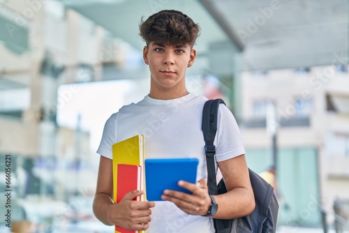Young hispanic teenager student using touchpad holding books at university