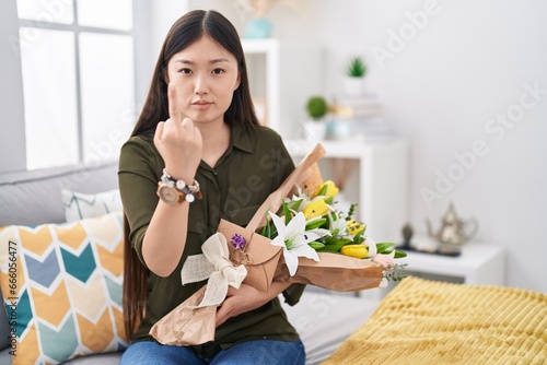 Chinese young woman holding bouquet of white flowers showing middle finger  impolite and rude fuck off expression