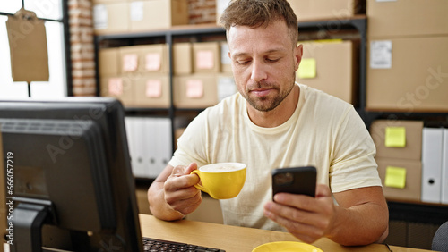 Young man ecommerce business worker using smartphone drinking coffee at office