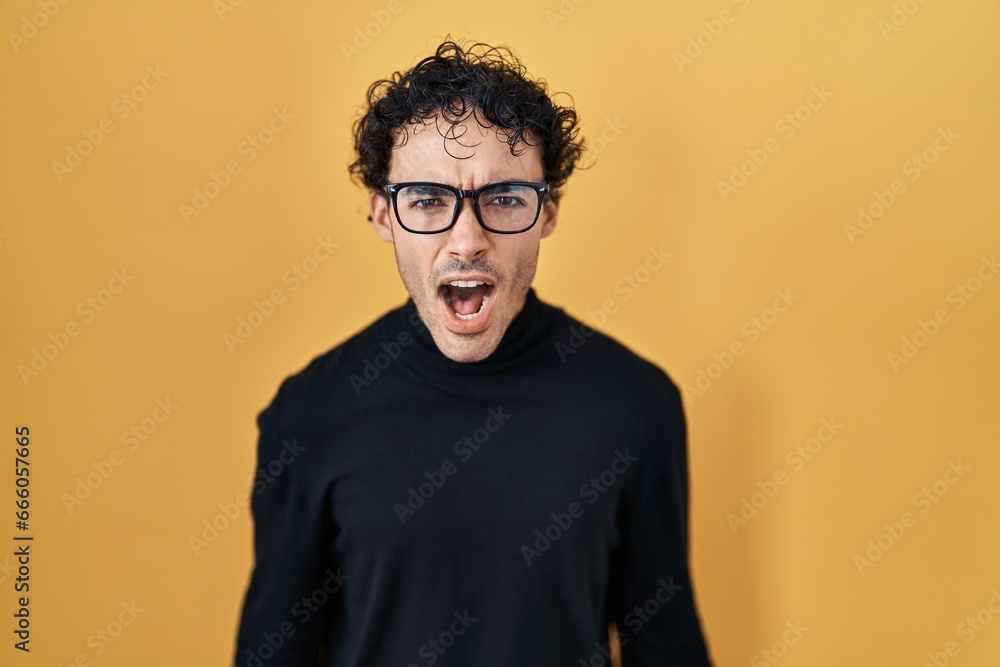 Hispanic man standing over yellow background angry and mad screaming frustrated and furious, shouting with anger. rage and aggressive concept. Hispanic man standing over yellow background angry and mad screaming frustrated and furious, shouting with anger. rage and aggressive concept.