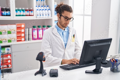 Young hispanic man pharmacist using computer at pharmacy