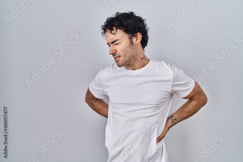 Hispanic man standing over isolated background suffering of backache, touching back with hand, muscular pain