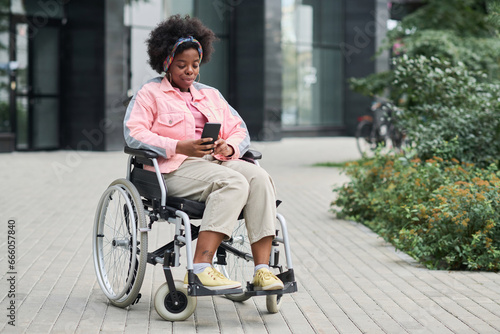 African American woman with disability sitting on wheelchair and using smartphone outdoors