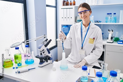 Young caucasian woman scientist pouring liquid on test tube at laboratory