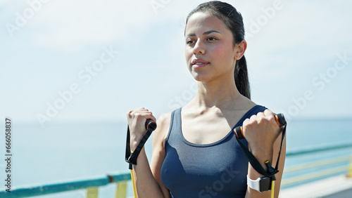 Young beautiful hispanic woman using elastic band training at seaside