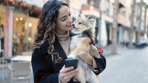 Young hispanic woman with dog smiling confident using smartphone at street