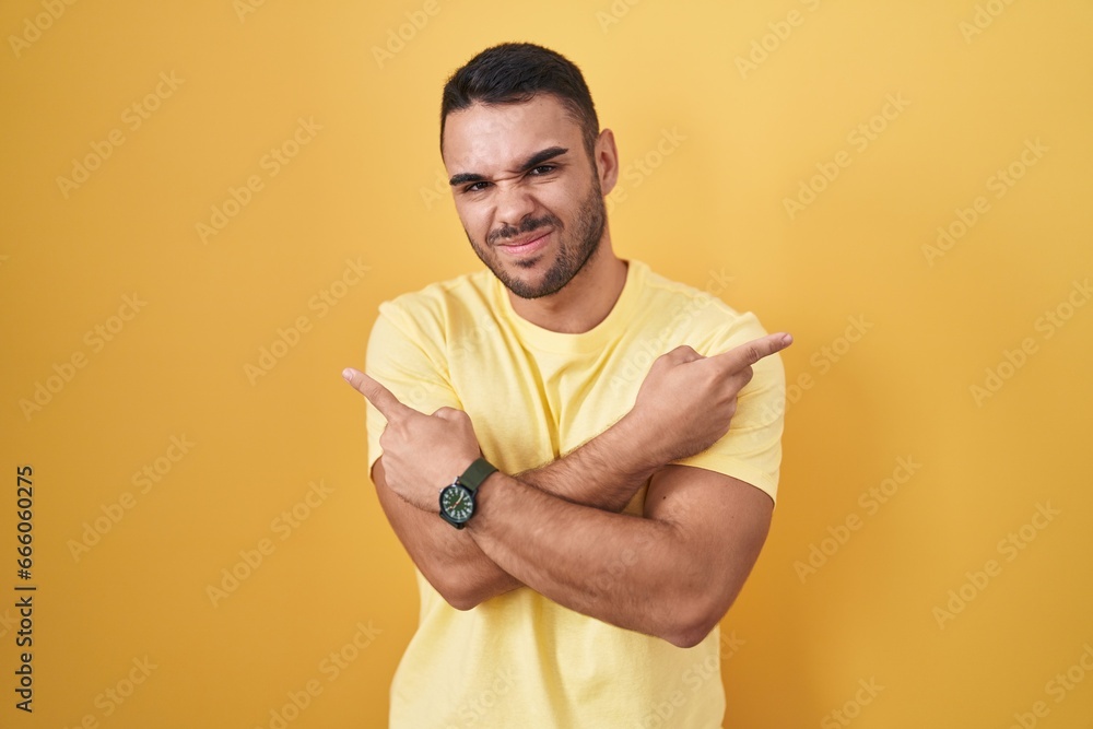 Young hispanic man standing over yellow background pointing to both sides with fingers, different direction disagree Young hispanic man standing over yellow background pointing to both sides with fingers, different direction disagree
