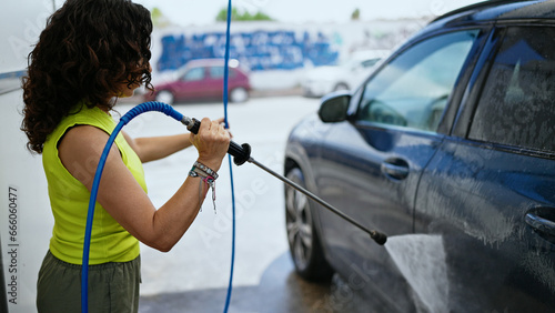 Middle age hispanic woman washing car with pressure washer at car wash station