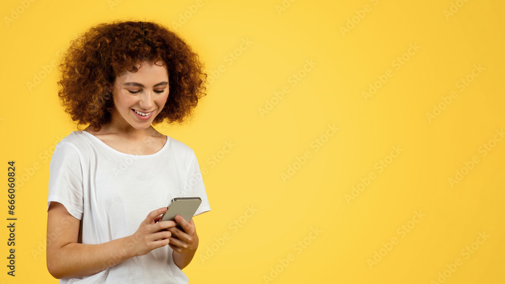 Happy young woman chatting on phone, typing message on device, isolated on yellow background Happy young woman chatting on phone, typing message on device, isolated on yellow background