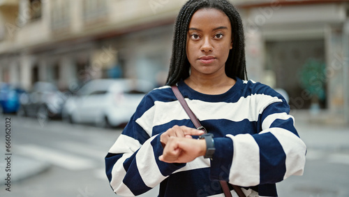 African american woman looking at the watch waiting with serious expression at street