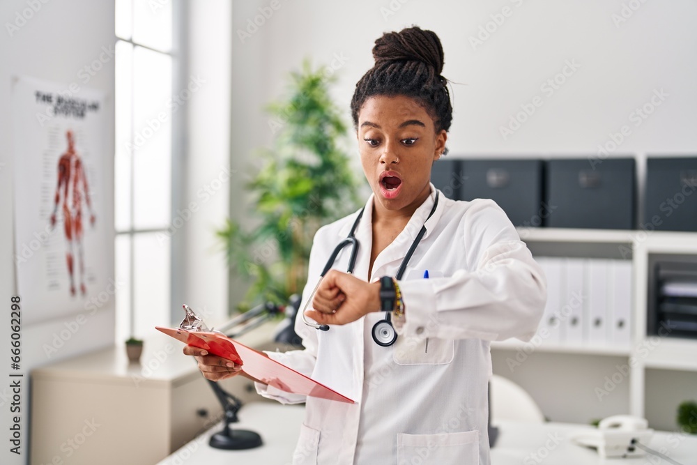 Φωτογραφία Young african american with braids wearing doctor uniform looking at the watch afraid and shocked with surprise and amazed expression, fear and excited face