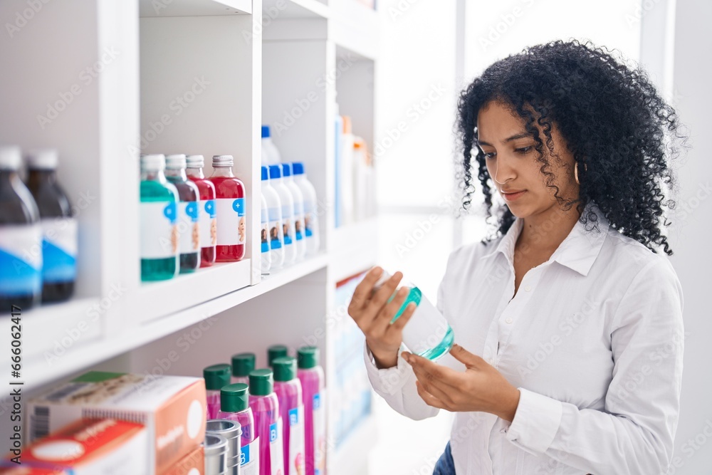 Young hispanic woman customer holding bottle on shelving at pharmacy Young hispanic woman customer holding bottle on shelving at pharmacy