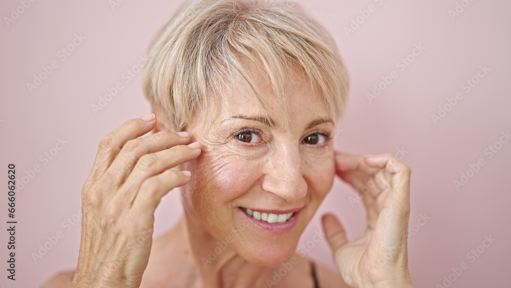Middle age blonde woman smiling confident caring skin face over isolated pink background Middle age blonde woman smiling confident caring skin face over isolated pink background