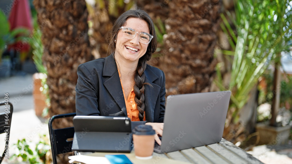 Young beautiful hispanic woman business worker using laptop and touchpad sitting on table at coffee shop terrace Young beautiful hispanic woman business worker using laptop and touchpad sitting on table at coffee shop terrace