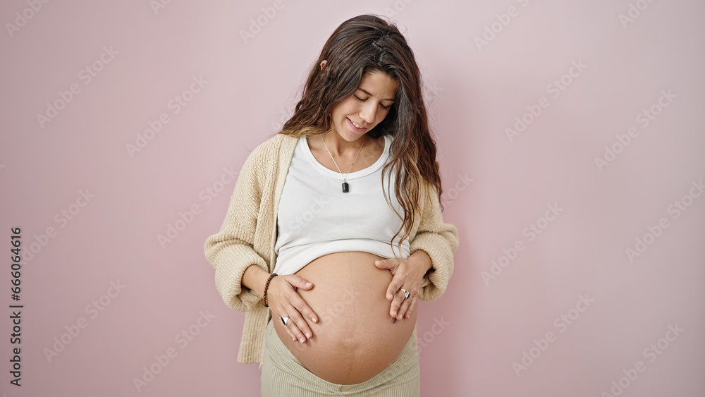Young pregnant woman smiling confident massaging belly over isolated pink background Young pregnant woman smiling confident massaging belly over isolated pink background