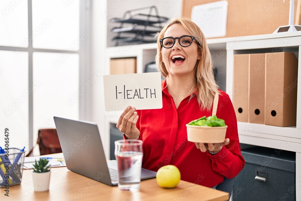 Φωτογραφία Blonde woman working at the office eating healthy food smiling and laughing hard out loud because funny crazy joke
