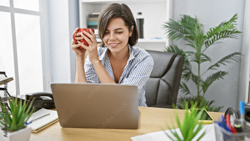Confident young hispanic woman boss, with beautiful smile and short hair, happily working early morning at her office desk, drinking coffee while using her laptop for online business success. Confident young hispanic woman boss, with beautiful smile and short hair, happily working early morning at her office desk, drinking coffee while using her laptop for online business success.