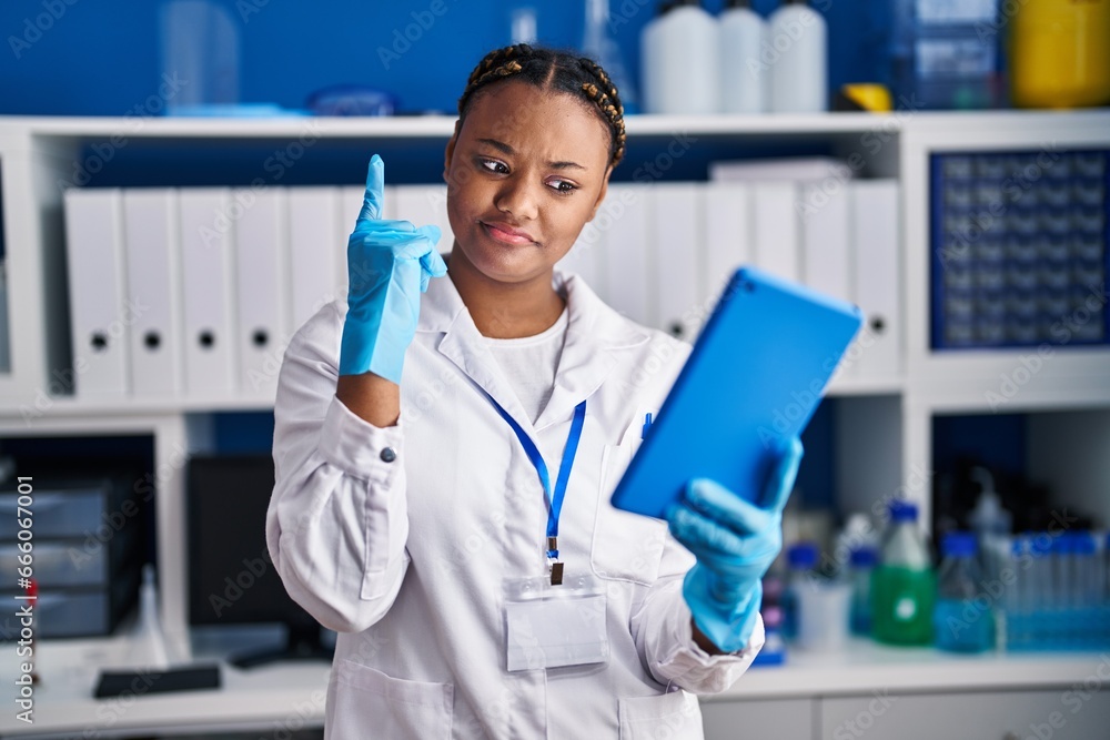 African american woman with braids working at scientist laboratory doing video call with tablet smiling with an idea or question pointing finger with happy face, number one African american woman with braids working at scientist laboratory doing video call with tablet smiling with an idea or question pointing finger with happy face, number one
