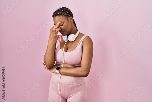 African american woman with braids wearing sportswear and headphones tired rubbing nose and eyes feeling fatigue and headache. stress and frustration concept.
