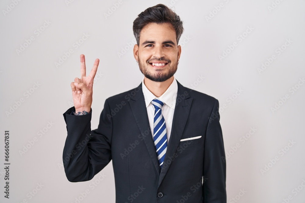 Young hispanic man with tattoos wearing business suit and tie showing and pointing up with fingers number two while smiling confident and happy. Young hispanic man with tattoos wearing business suit and tie showing and pointing up with fingers number two while smiling confident and happy.