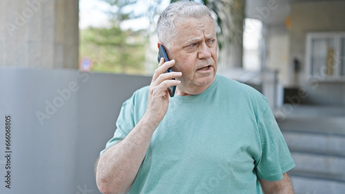 Middle age grey-haired man talking on smartphone with serious expression at street