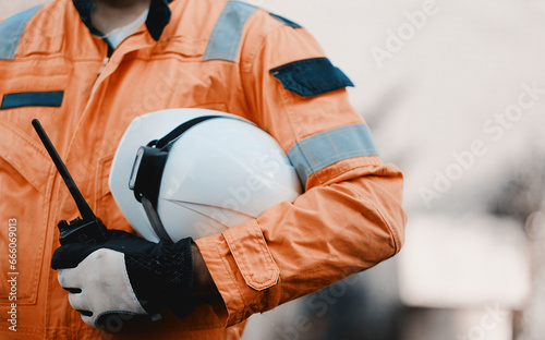 Fit Man Holding Safety Helmet With A Heavy-Duty Light And Walkie Talkie Radio Station In A Hand Wearing An Orange Uniform photo