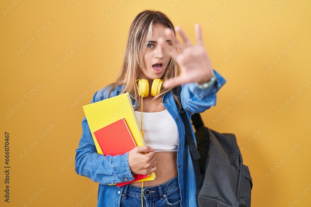 Young blonde woman wearing student backpack and holding books doing stop gesture with hands palms, angry and frustration expression Young blonde woman wearing student backpack and holding books doing stop gesture with hands palms, angry and frustration expression