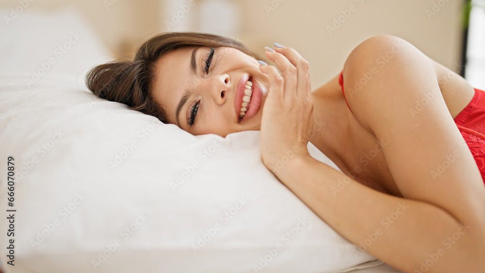 Fototapeta premium Young caucasian woman wearing lingerie lying on bed smiling at bedroom