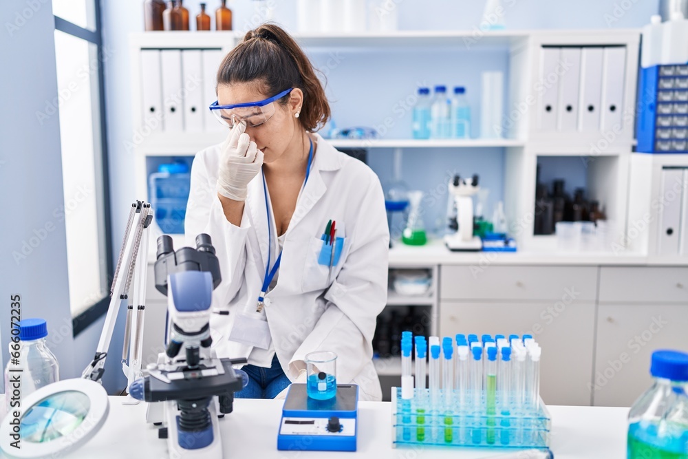 Young hispanic woman working at scientist laboratory tired rubbing nose and eyes feeling fatigue and headache. stress and frustration concept. Young hispanic woman working at scientist laboratory tired rubbing nose and eyes feeling fatigue and headache. stress and frustration concept.