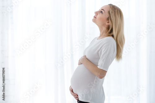 A young blonde pregnant woman stands by the window and strokes her belly in the rays of the morning sun. tender photo session of the expectant mother. pregnant woman in a short top and shorts Free Download A young blonde pregnant woman stands by the window and strokes her belly in the rays of the morning sun. tender photo session of the expectant mother. pregnant woman in a short top and shorts - GFXLoad