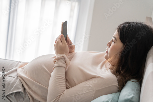 Pregnant asian woman holding smartphone at home using mobile app