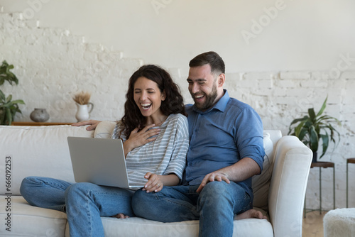 Cheerful excited married couple celebrating success, win, profit at laptop, looking, staring at display, laughing in amazement, surprise, getting good awesome news from video call