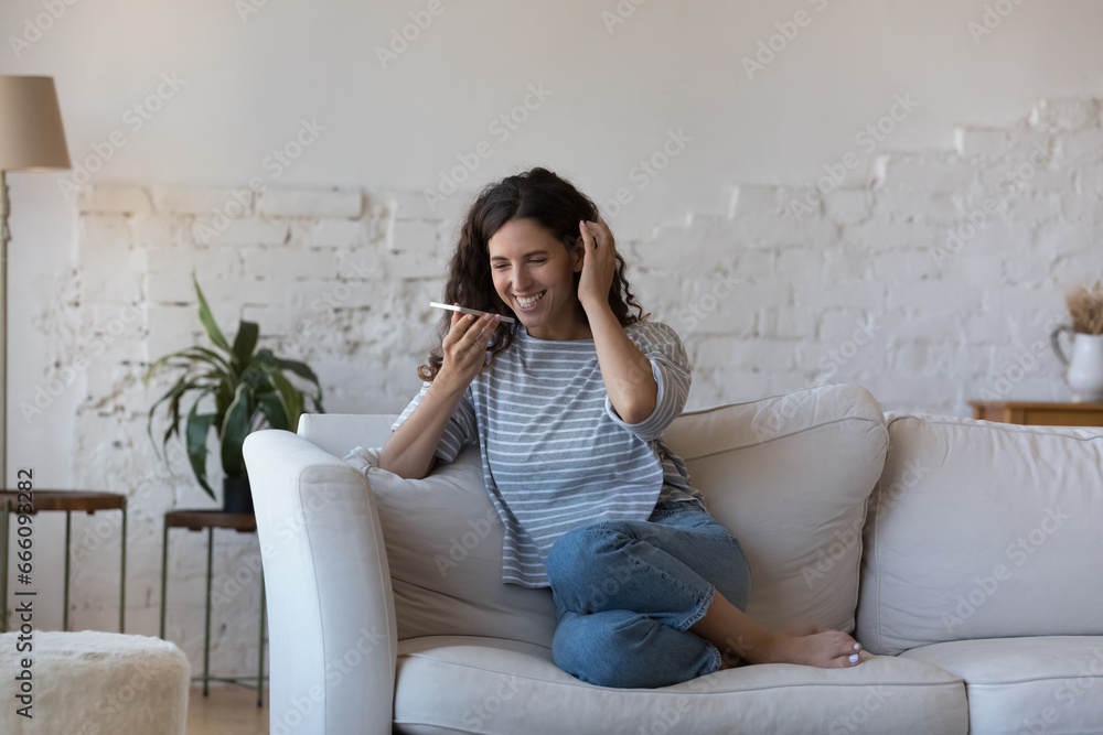 Happy cheerful cellphone user woman talking on speaker at home, recording audio voice message, dictating commands to virtual assistant, talking at mic, holding smartphone at mouth, laughing