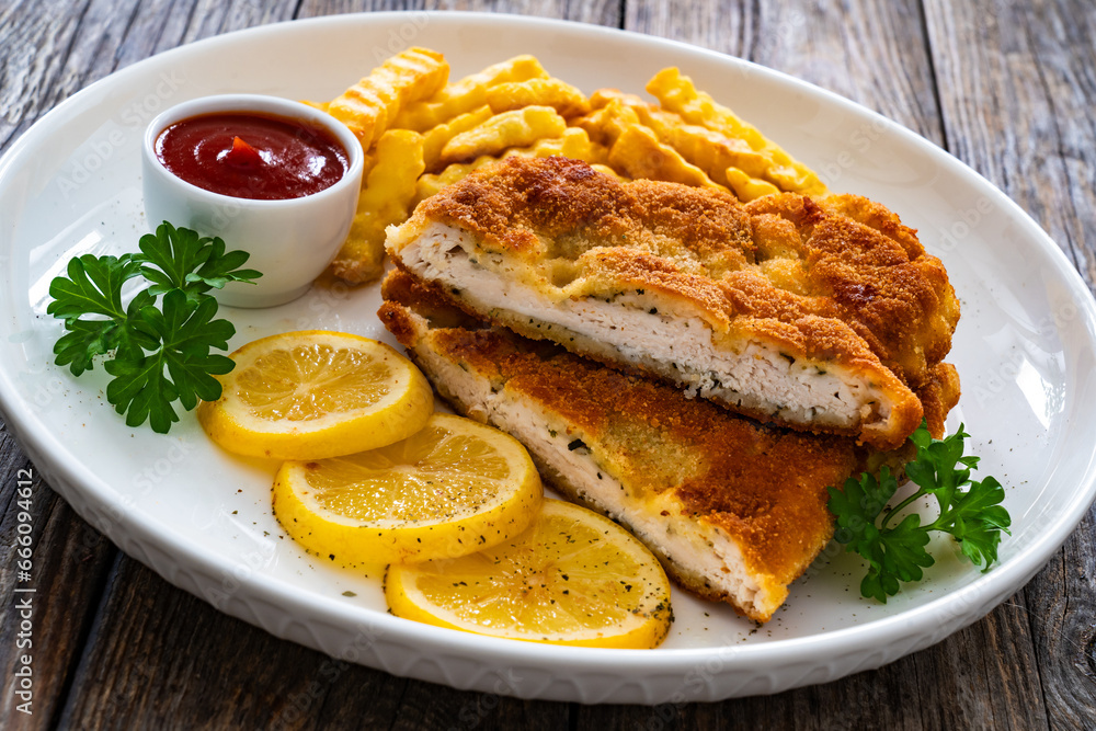 Crispy breaded seared chicken cutlet with French fries, lemon and fresh vegetables on wooden table
Crispy breaded seared chicken cutlet with French fries, lemon and fresh vegetables on wooden table