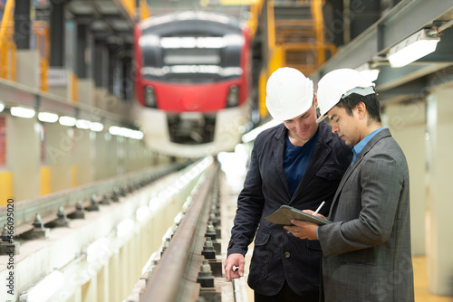 Two businessmen inspect rail work to reserve equipment for use in repairing tracks and machinery of the electric train transportation system.