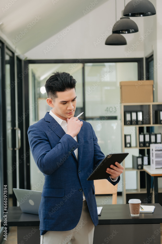 Confident Asian man with a smile standing holding notepad and tablet at the modern office. Confident Asian man with a smile standing holding notepad and tablet at the modern office.
