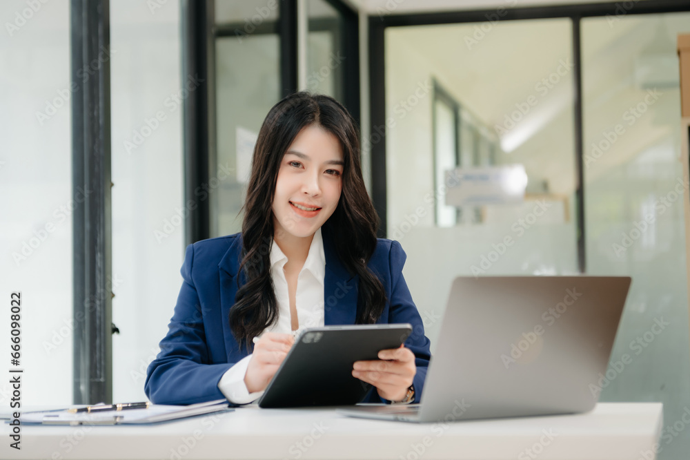 Confident business expert attractive smiling young woman typing laptop ang holding digital tablet on desk in creative office. Confident business expert attractive smiling young woman typing laptop ang holding digital tablet on desk in creative office.