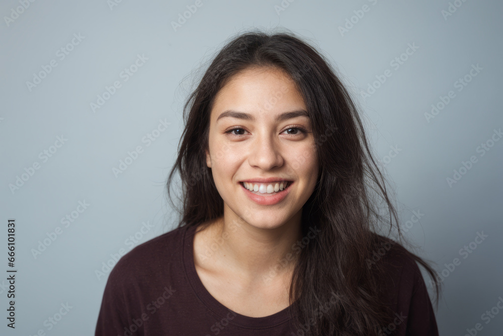 Fototapeta premium Everyday people. A smiling woman with long brown straight hair over her shoulder. Wearing a brown tshirt. Pretty woman. University student. On a light grey studio background. Portrait.