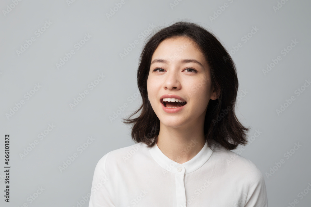 Everyday people. A happy asian woman laughing. Black straight hair to her shoulders. Wearing a white shirt. Pretty woman. University student. On a light grey studio background. Portrait. Everyday people. A happy asian woman laughing. Black straight hair to her shoulders. Wearing a white shirt. Pretty woman. University student. On a light grey studio background. Portrait.